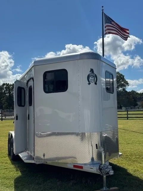 White Adam horse trailer parked on grass with an American flag flying behind it.